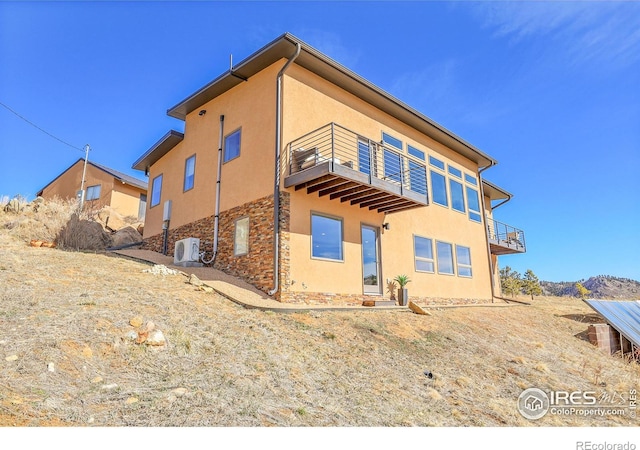 rear view of house featuring stone siding, a balcony, and stucco siding