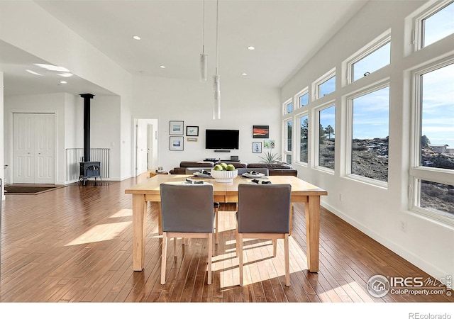 dining area with recessed lighting, a towering ceiling, baseboards, wood-type flooring, and a wood stove