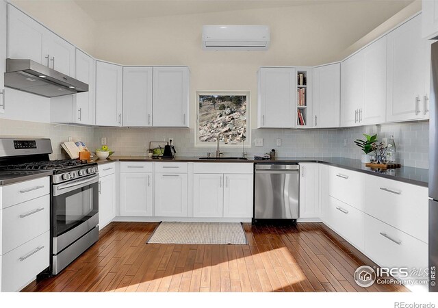 kitchen with stainless steel appliances, a sink, an AC wall unit, range hood, and dark countertops