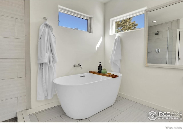 bathroom featuring a soaking tub, baseboards, and tiled shower