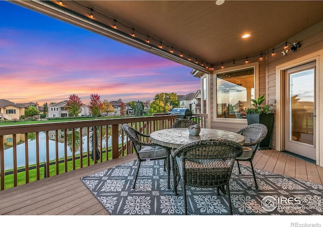 wooden deck featuring grilling area, outdoor dining area, a water view, and a residential view