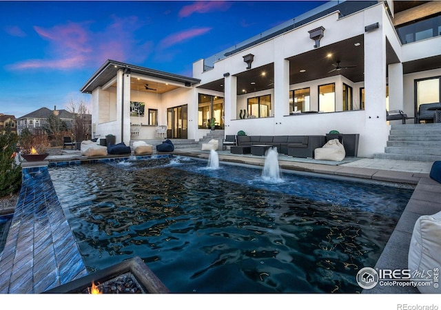 back of house at dusk featuring outdoor lounge area, a ceiling fan, and stucco siding