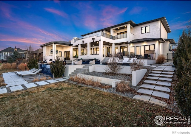 back of property at dusk with a patio, a balcony, and stucco siding