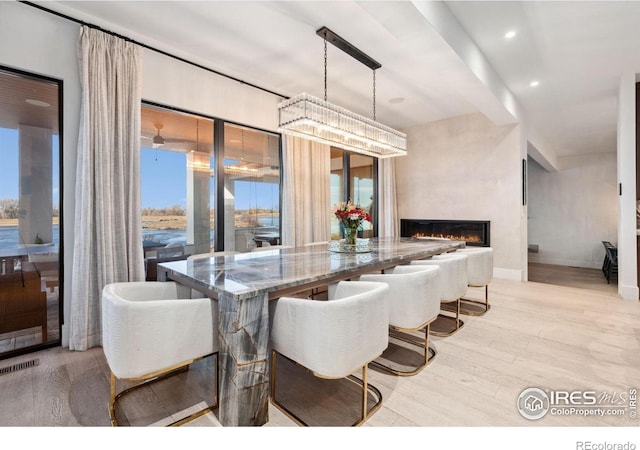 dining room with plenty of natural light, light wood-style floors, a lit fireplace, and visible vents