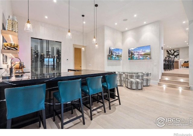 kitchen with recessed lighting, a sink, light wood-type flooring, dark countertops, and pendant lighting