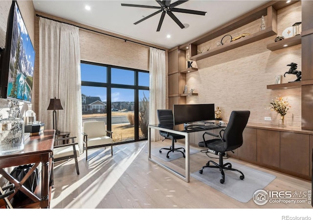 office space featuring ceiling fan, light wood-style flooring, and a towering ceiling