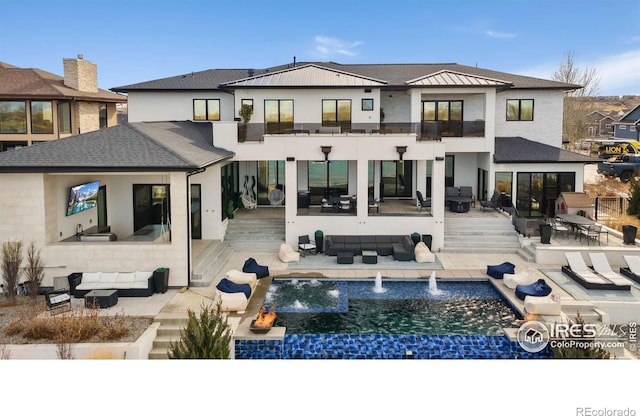 rear view of house with a balcony, a patio area, an infinity pool, and outdoor lounge area