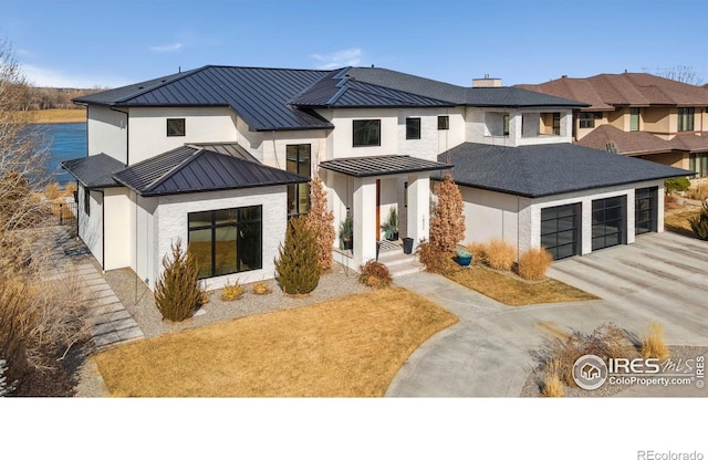 view of front facade featuring a standing seam roof, metal roof, an attached garage, concrete driveway, and a chimney