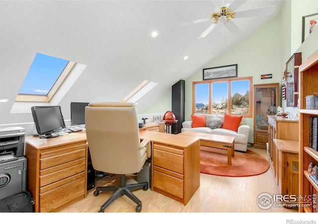 home office with ceiling fan, vaulted ceiling with skylight, and light wood-type flooring