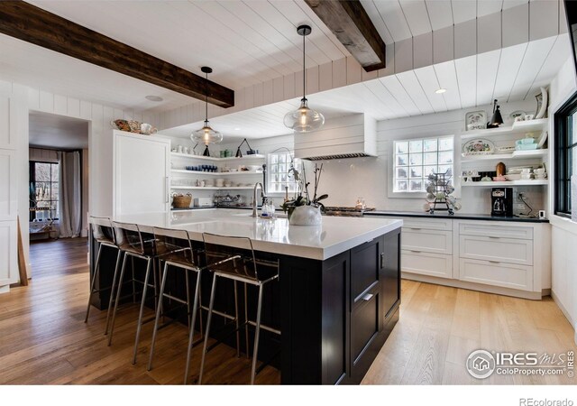 kitchen with dark cabinets, beam ceiling, light wood-type flooring, open shelves, and a sink