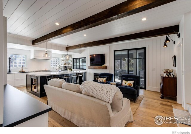 living area featuring recessed lighting, a fireplace, light wood-type flooring, beam ceiling, and indoor wet bar