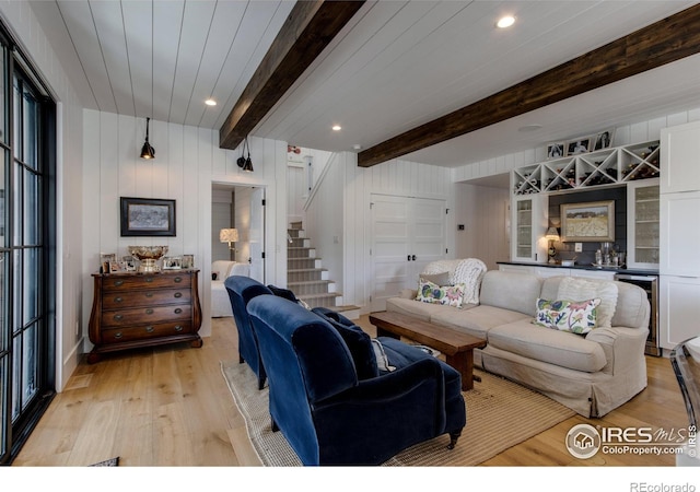 living area with light wood-type flooring, stairway, a dry bar, and beam ceiling