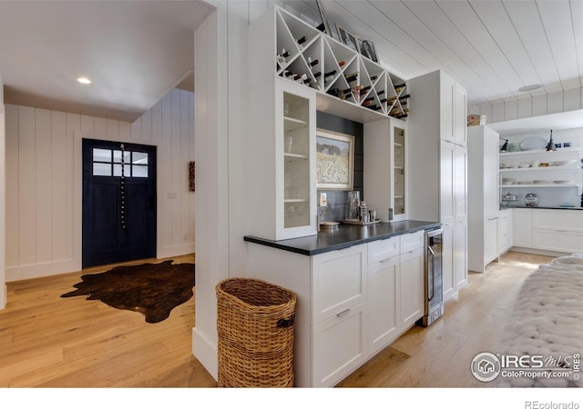 kitchen with light wood-style floors, dark countertops, beverage cooler, and white cabinets