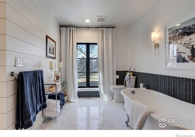 bathroom featuring a wainscoted wall, a freestanding tub, and visible vents