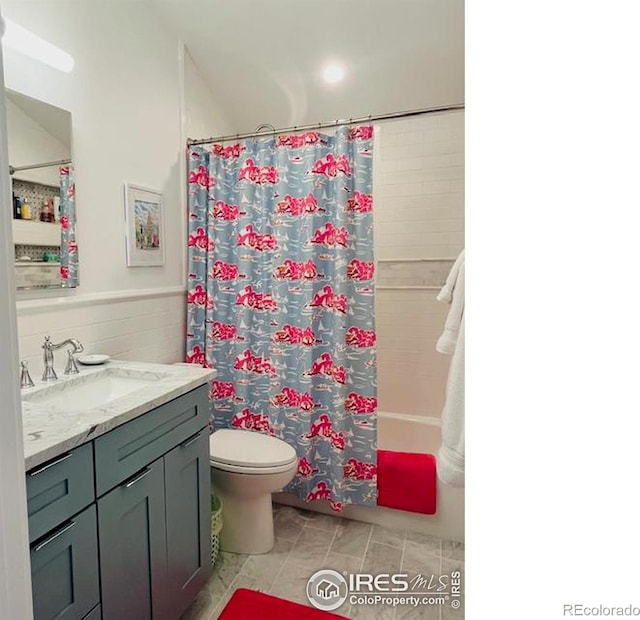 bathroom featuring tile walls, shower / bath combination with curtain, toilet, wainscoting, and vanity