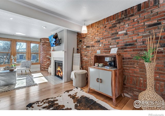 living room featuring a warm lit fireplace, light wood-style flooring, and brick wall