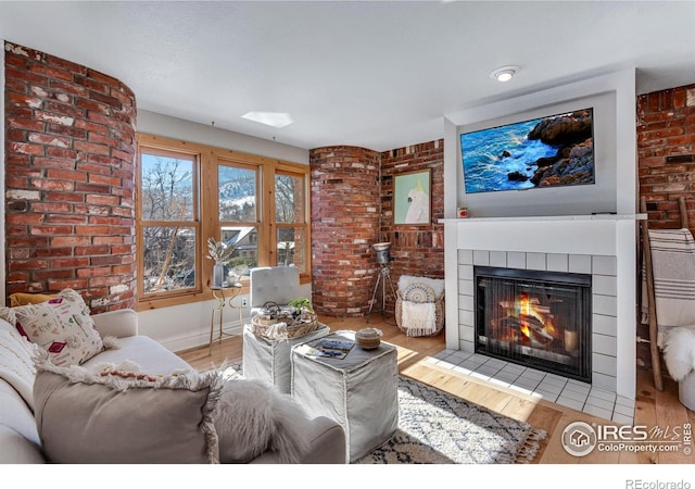 living room with a fireplace with flush hearth, brick wall, wood finished floors, and baseboards