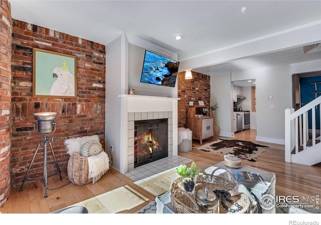 living room with stairs, a tile fireplace, wood finished floors, and baseboards