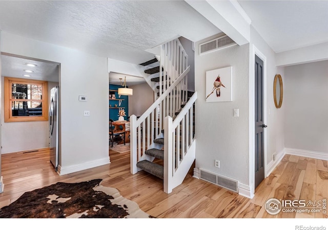 stairs with a textured ceiling, hardwood / wood-style flooring, and visible vents