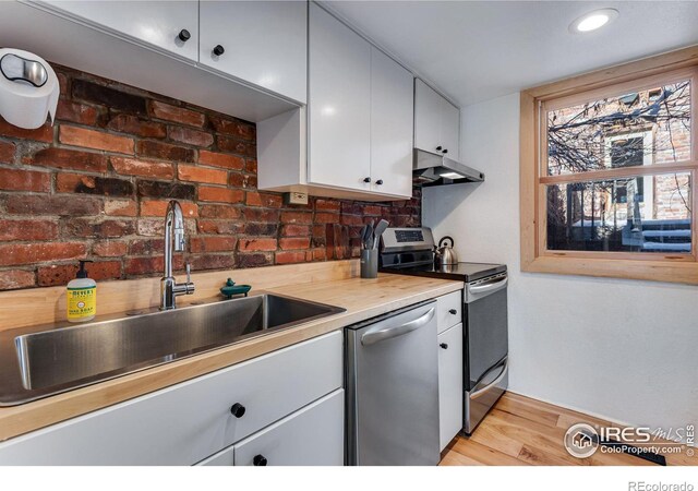 kitchen with stainless steel appliances, light countertops, light wood-style flooring, a sink, and under cabinet range hood