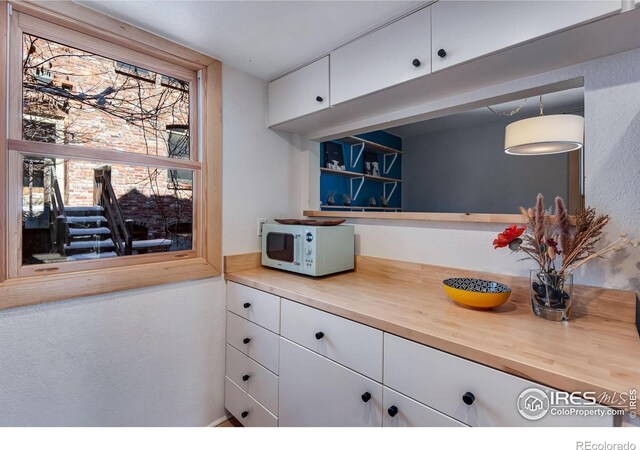 interior space with butcher block counters, white cabinets, a textured wall, and white microwave