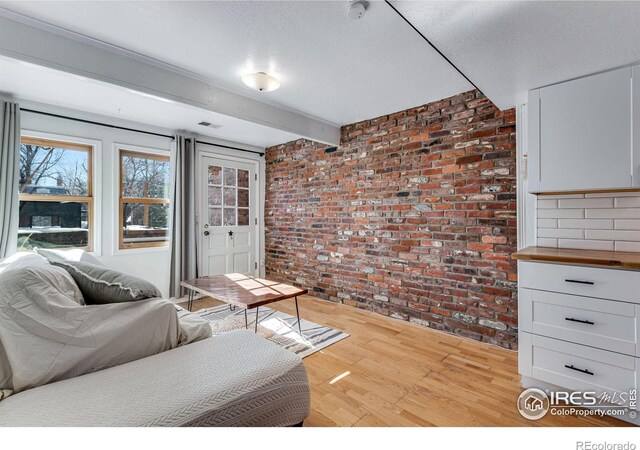 living area featuring visible vents, brick wall, beamed ceiling, and light wood-style flooring