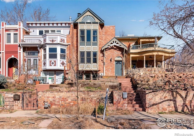 view of front of home featuring brick siding, a gate, and a balcony