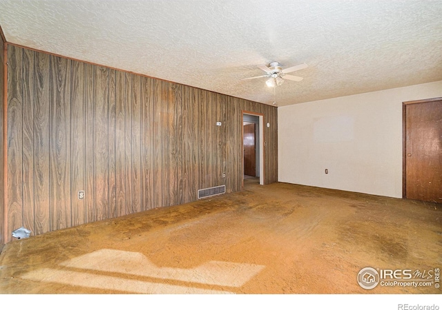 unfurnished room with wooden walls, visible vents, ceiling fan, carpet, and a textured ceiling