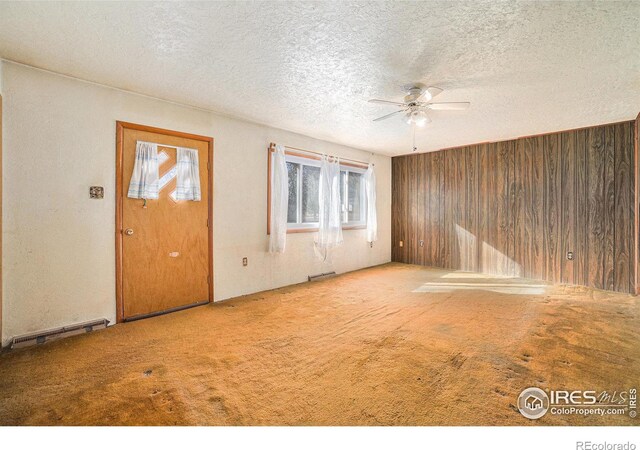 carpeted empty room featuring wood walls, ceiling fan, visible vents, and a textured ceiling