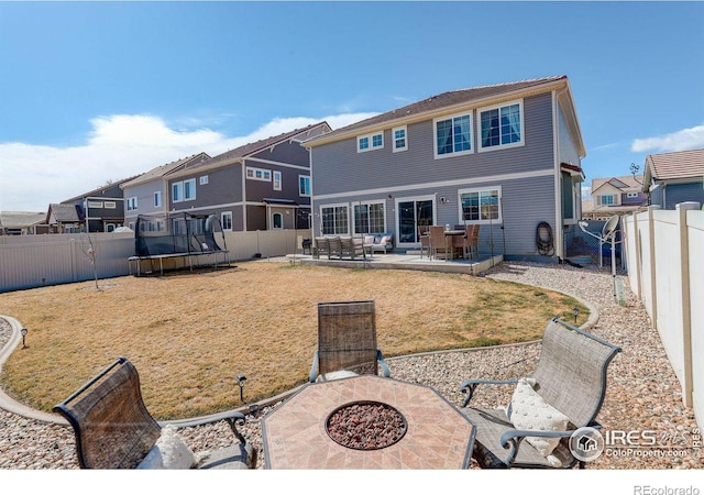 rear view of property featuring an outdoor fire pit, a patio, a fenced backyard, a trampoline, and a yard