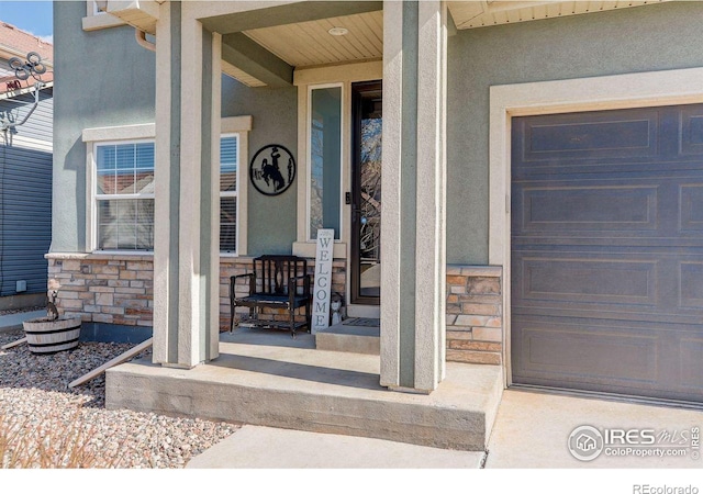 doorway to property featuring covered porch, stone siding, a garage, and stucco siding