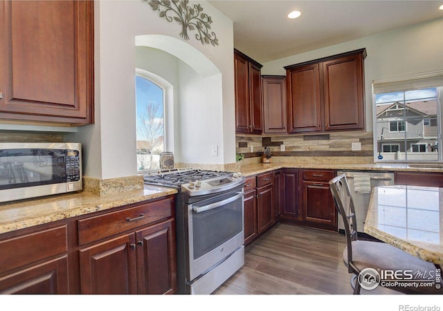 kitchen with light stone counters, recessed lighting, stainless steel appliances, dark wood-type flooring, and backsplash