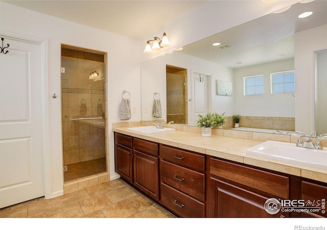 bathroom featuring visible vents, a sink, a shower stall, and double vanity