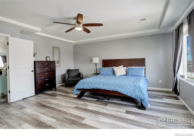 bedroom featuring a tray ceiling, visible vents, light wood-style flooring, and baseboards