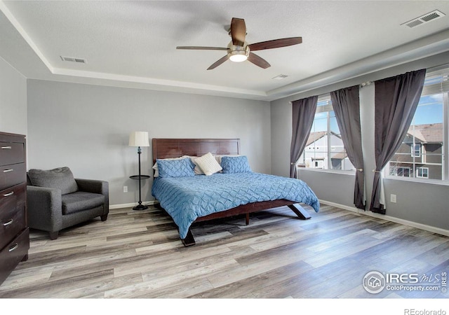 bedroom featuring a tray ceiling, light wood-style flooring, visible vents, and baseboards