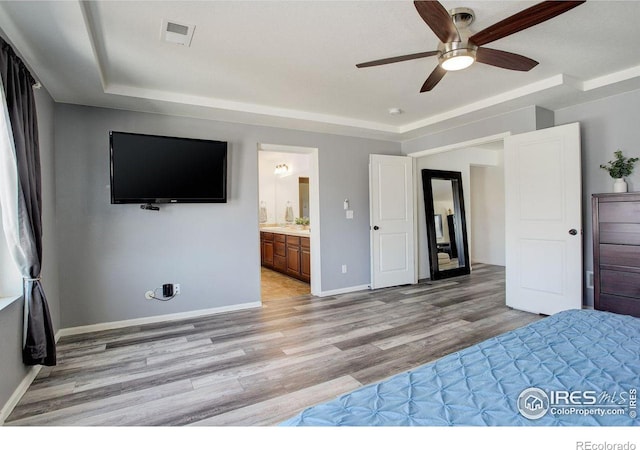 unfurnished bedroom featuring baseboards, visible vents, ensuite bath, ceiling fan, and light wood-type flooring