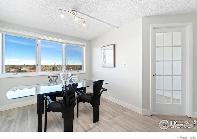 dining area with a textured ceiling, a wealth of natural light, light wood-style flooring, and baseboards