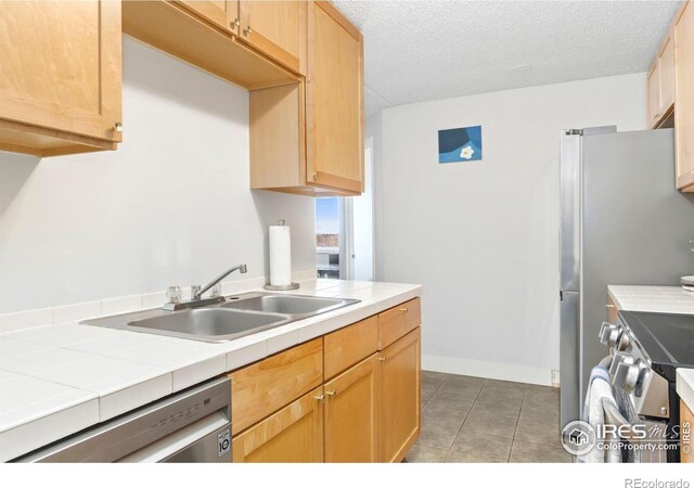 kitchen with tile countertops, tile patterned flooring, stainless steel appliances, a textured ceiling, and a sink