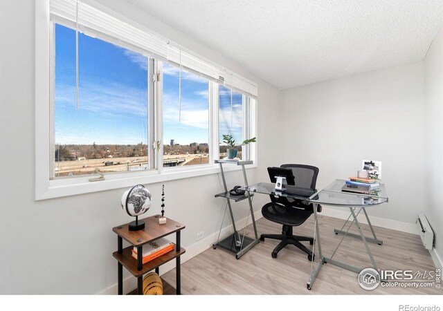 home office featuring a textured ceiling, baseboard heating, wood finished floors, and baseboards