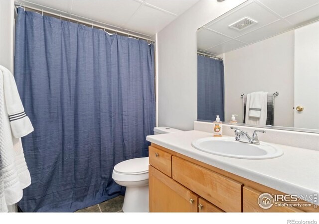 bathroom with visible vents, a drop ceiling, toilet, tile patterned floors, and vanity