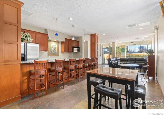 dining space featuring stone finish flooring, visible vents, decorative columns, and a textured ceiling