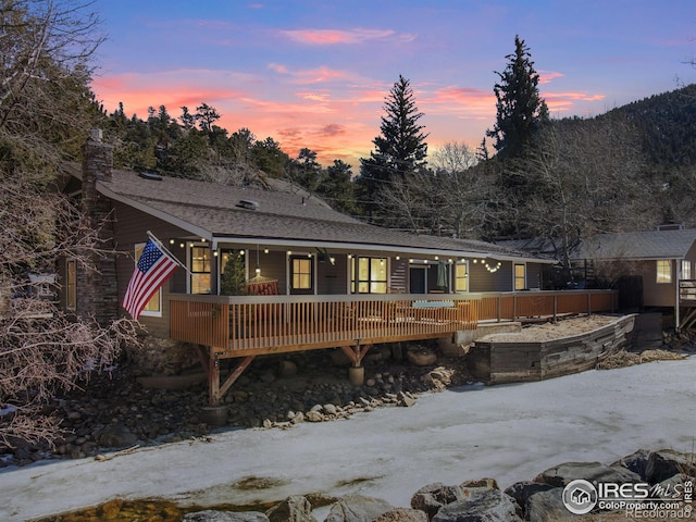 back of property at dusk with a shingled roof, a chimney, and a wooden deck