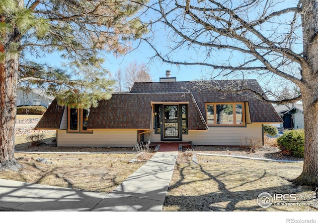 a-frame style home with roof with shingles, mansard roof, and a chimney