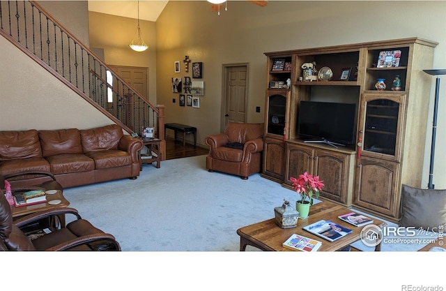 carpeted living room featuring high vaulted ceiling, stairway, and a ceiling fan