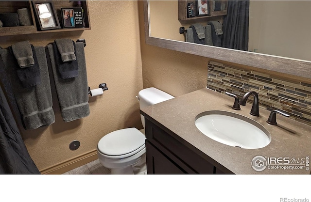 bathroom featuring toilet, a textured wall, backsplash, and vanity