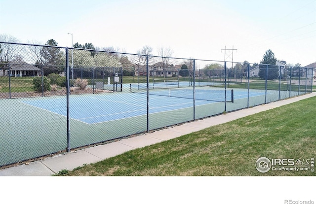 view of tennis court with a lawn and fence