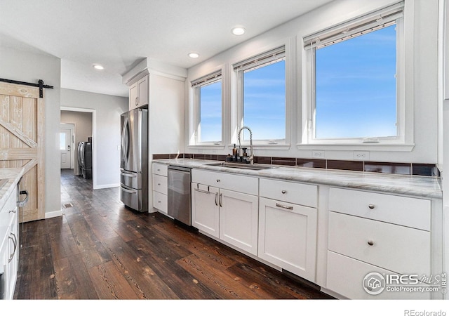 kitchen featuring dark wood finished floors, a barn door, appliances with stainless steel finishes, white cabinets, and a sink