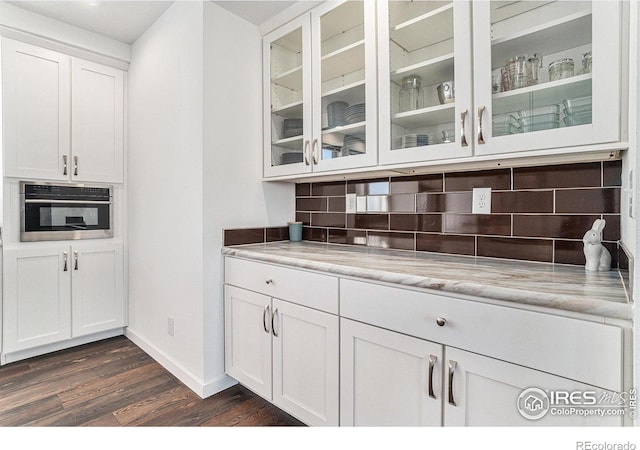 kitchen featuring dark wood-style flooring, backsplash, glass insert cabinets, white cabinetry, and oven