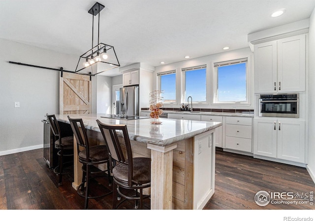 kitchen with a center island, dark wood-style flooring, stainless steel appliances, a barn door, and light stone countertops