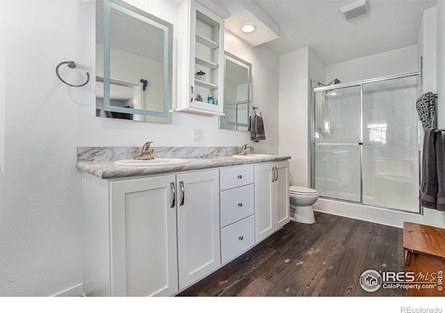 bathroom with wood finished floors, a sink, toilet, and a shower stall